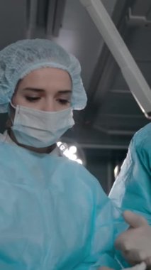 Genç bir bayan doktor ve onun iş arkadaşı, yetişkin bir profesyonel cerrah modern bir hastanenin ameliyathanesinde ameliyat için ekipman hazırlıyorlar. Orta yavaş çekim. Dikey çekim.