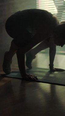Spor salonunda yoga yapan sportif bir kızın silüeti vinç pozisyonunda duruyor. Salonun içinde yavaş çekim geniş çaplı. Dikey çekim.