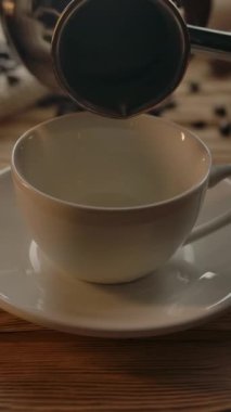 Kadınlar kahve için Cezve 'den gelen kahveyi ahşap bir masada bir fincana doldurur. Arka planda kahve çekirdekleri, jüt kumaş, kurabiyeler. Dikey çekim.