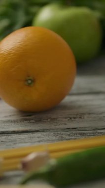 Tanınmayan kişi, organik meyve ve sebzelerin arasında tahta masaya taze portakal itiyor. Dikey çekim.