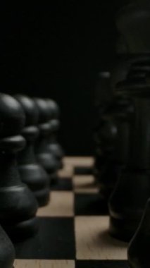 Siyah satranç figürleri başlangıç pozisyonunda oyun konseptine hazır. Satranç figürleri ve piyonlar arasında kayan geniş bir makro çekim. Dikey çekim.