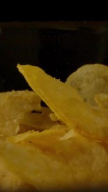 Karanlık odada cam kasenin üzerine kızarmış patates cipsi düşüyor. Dikey çekim.