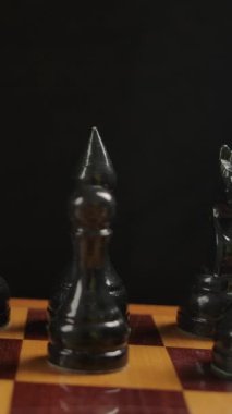 Başlangıç pozisyonu olarak dama tahtasındaki tahta siyah satranç taşlarını geniş açıyla çek. Kamera makro doli hareketi Dikey çekim.