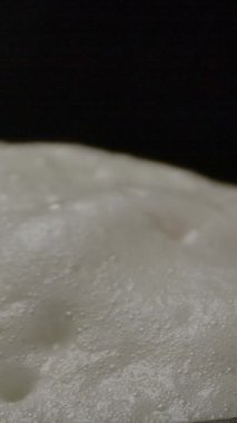 Koyu bardaki cam bardak dolusu taze biranın üzerinde köpüren ve köpüren yumuşak beyaz köpükten uzaklaşan kamera. Dikey çekim.