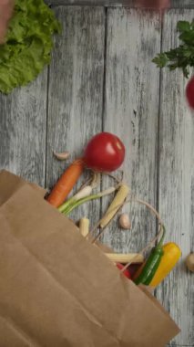 Yukarıdan tanınmayan insanlar mutfaktaki kereste masasındaki alışveriş poşetinden taze sebzeler alıyorlar. Dikey çekim.