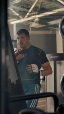 Kendine güvenen bir sporcunun turntable 'dan kum torbasını tekmelerken orta boy fotoğrafı. Mavi pantolonlu ve siyah tişörtlü profesyonel Kafkas sporcusu boks veya kickboksör eğitimi alıyor. Dikey çekim.