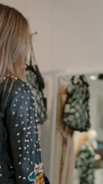 Moda mağazasında son moda günlük kıyafetlerle dolaşan, sonra durup arkasını dönen, mor topuklu ayakkabıları giyen ve arkadaşına sarışını veren kadınların arka plan görüntüleri.