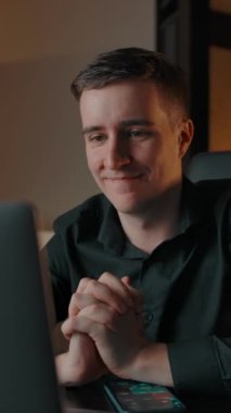 Bir adam konferansta evdeki laptop kamerasından gülümsüyor. Kafkasyalı genç bir adam internetteki engeli seve seve dinler ve iletişim kurar. Dikey çekim.