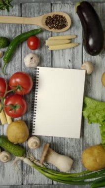 Ahşap mutfak tezgahına sebzelerle ve baharatlı kaşıkla ağır çekimde yemek pişirme kitabının en üst görüntüsü. Dikey çekim.