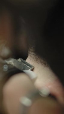 Modern berber dükkanında çalışırken yetişkin bir adamın sakalını tıraş etmek için düz jilet ve doku kullanan eldivenli sarışının son derece yakın plan fotoğrafı. Makro Dikey Çekim.