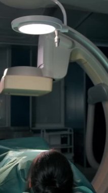 Avrupalı ve Afrikalı iki cerrah ameliyata hazırlanıyor. Genç bayan hasta ameliyat masasında yatıyor. Dikey çekim.