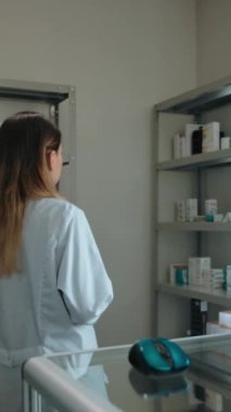 Kendine güvenen güzel bir beyaz kadın eczacının portresi. Raflardaki ilaçların bulunup bulunmadığını gözlemlemek ve kontrol etmek ve kameraya gülümseyen arkadaşça bir bakış. Eczane içi