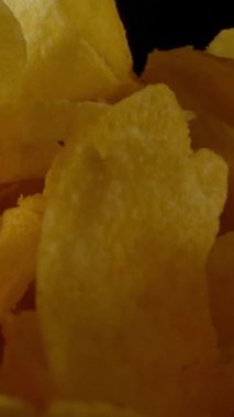 Yakın plan, karanlık odada dönen cam kasenin içinde taze patates cipsi. Dikey çekim.