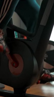 Spor salonunda bisikletle pedal çeviren aktif bir sporcu. Güç konseptin ayaklarına yüklenir. Ayaktan yüze doğru dikey dönüş. Dikey çekim.