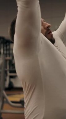 Erkek, göğüs kasları ve üst bloktaki kaslar üzerinde egzersiz yapıyor. Beyaz tenli güçlü kaslı adam, panoramik çekim, etrafta uçan kamera. Dikey çekim.