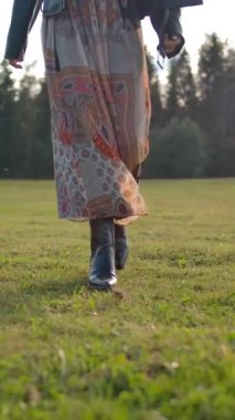 Tanımlanamayan bir kadının uzun elbiseli yeşil çimlerde ağır çekimde ve gerçek zamanlı yürürken kırsal kesimde çiftlikte dikey çekim yaparken görüntüsü..