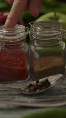 Kamera, taze olgun sebzelerin ve erkek parmağı mutfak masasında baharat seçen çeşitli baharatların yanından geçti. Dikey çekim.