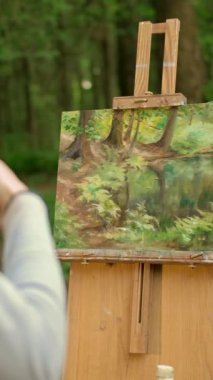 Çekici esmer kadın ormandaki açık havada manzara resmediyor ve fotoğraf çekiyor. Arkadan bak. Kadın sanatçı, resminin resmini akıllı telefondan çekiyor. Dikey çekim.