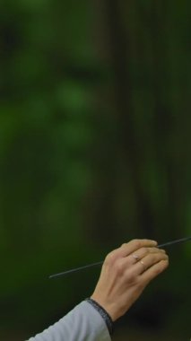 Ormanın doğası üzerine güzel bir manzara çizen bir kadın. Esmer bir kız işini bitirmek için tuvalin üzerinde fırça sürüyor. Orta açı. Dikey çekim.