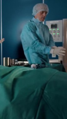 Özel cüppeli iki deneyimli cerrah hastaların ameliyathanesine gelir. Yetişkin erkek ve genç bayan asistan tıbbi operasyon için hazır. Dikey çekim.