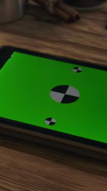 Yatay yeşil ekran tableti ahşap masanın yanındaki sehpanın üzerinde. Dönen tahta masa yüzeyini izlemeye hazırız. Dikey çekim.