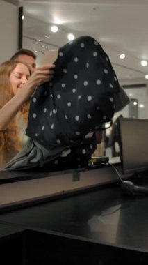 Sevgi dolu bir çift şık bir mağazadaki kasiyere bez veriyor. Paralı kumaş ve ayakkabı dükkanında çalışan yakışıklı sarışın genç bir satıcı. Ağır çekimde ağır çekimde ağır çekimde. Dikey çekim.
