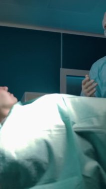 Profesyonel bir yetişkin cerrah, ameliyat odasında ciddi bir ameliyattan önce hastaya lokal anestezi altında danışmanlık yapar ve sakinleştirir. Dikey çekim.