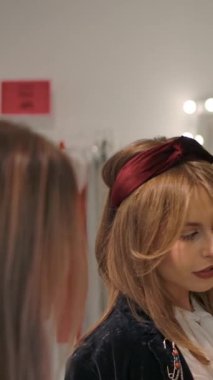 Yukardan aşağı eğil ve sonra yeni moda ve yeni kıyafet seçen mutlu bin yıllık kadınların sağa doğru çekimini yap, askıların yanında dururken ve elbise mağazasındaki elbise askılarına yavaşça dokunurken