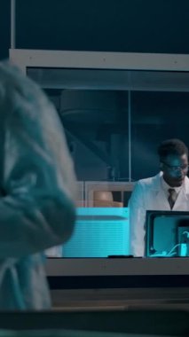 Profesyonel, koyu tenli, Afro-Amerikalı bir doktor, meslektaşlarının cam pencerenin arkasındaki ameliyatlarını denetliyor ve kontrol odasından emirler veriyor. Dikey çekim.