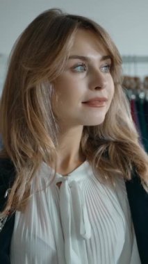 Yavaş çekim, çekici genç bayan müşterinin sağa, moda mağazasında dikilip başka tarafa bakıyor ve kameraya bakıp gülümsüyor. Dikey çekim.