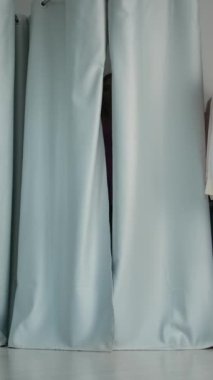 Modern mağazada kıyafet denerken, giyinme odasının perdelerini çekip kameraya doğru yürüyen, şık giyimli genç bir kadın. Dikey çekim.