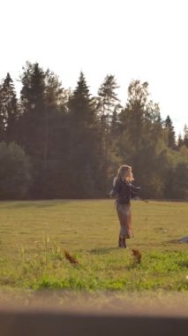 Güneşli bir günde çiftlikte dikey çekimde at ve ineklere doğru dönen ve yürüyen tasasız kadın..
