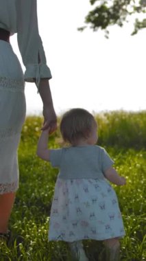 Beyaz rustik elbiseli annesiile el iyle tarlada yürüyen küçük kızın portresi. Bir buçuk yaşındaki kızı kameraya döner. Arka planda salıncaklar ile eski meşe ağacı. Günbatımı