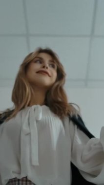 Moda kıyafetli genç bir bayanın trabzanda kıyafet çekmesi ve modern mağazada kıyafet seçerken kameraya gülümsemesi. Dikey çekim.