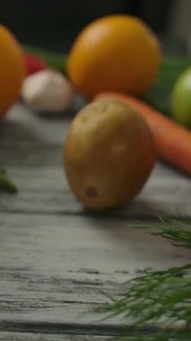 Tahta masanın üzerinde patates yuvarlama planı. Vejetaryen çiğ sebzeler, mantarlar ve kırsal masada yeşillik. Dikey çekim.