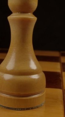 Piyon - Satranç figürü. Satranç tahtasına geniş açılı makro atış. Dama tahtasında siyah arkaplanlı beyaz satranç taşlarının üzerinde oldukça yakın bir hareketlilik var. Dikey çekim.