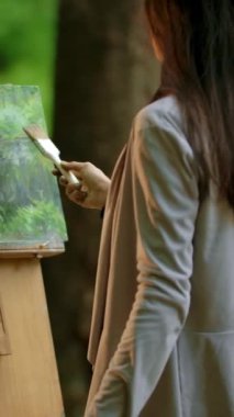 Yaz ormanlarında manzara çizen genç bir sanatçının arka orta manzarası. Çekici, ince esmer kız bir resim çiziyor. İşini bitiren bir sanat uzmanı. Bulutlu Aydınlatma