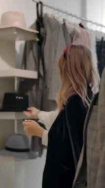 Moda mağazasında yeni kıyafet denemelerine yardım ederken zarif gri kareli takım elbiseli kadın müşteriye siyah şapka takan mutlu ve çekici bin yıllık çalışanın fotoğrafını çekiyorum. Dikey çekim.