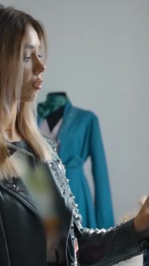 Moda kıyafetli genç bir bayan gülümsüyor ve hafta sonu alışveriş yaparken ağır çekimde yeni kıyafetler seçiyor. Dikey çekim.