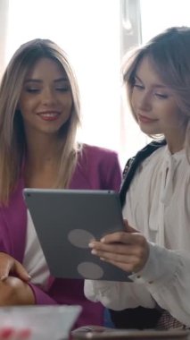 Sarışın kadın, haftasonu alışveriş yaparken kanepede otururken neşeli arkadaşına gülümseyip tableti online katalogla gösteriyor. Dikey çekim.
