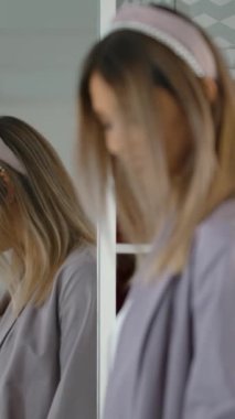 Hafta sonları modern mağazada vakit geçirirken şık kıyafetli, gülümseyen ve aynanın önünde dönen neşeli genç bir bayan. Dikey çekim.