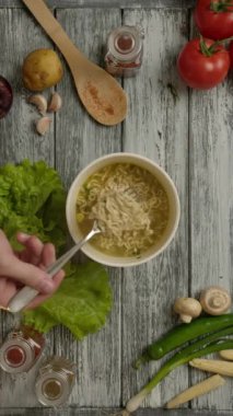 Tepede tanınmayan biri lezzetli erişte çorbasını karıştırıyor, sonra da mutfaktaki ahşap masada çatalı kaseden çıkarıyor. Dikey çekim.