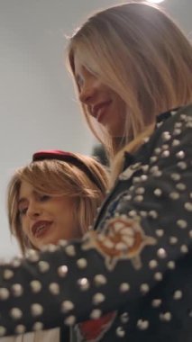 Gülümseyen ve şık kıyafetler seçen kadınların düşük açılı görüntüsü kıyafet mağazasında birlikte zaman geçirirken. Dikey çekim.