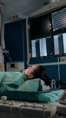 Doktor ameliyat için gerekli aletleri hazırlar. Genç bir bayan hasta ameliyat beklerken ameliyat masasında yatıyor. O, tıp alanında bir profesyoneldir. Dikey çekim.
