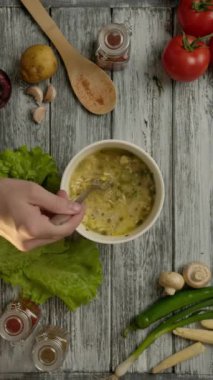 Taze sebze ve baharatların yanındaki ahşap masada lezzetli şehriye çorbası yapmak için çatal kullanan yüzü olmayan kişiden. Dikey çekim.