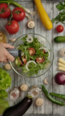 Kameranın üst görüntüsü, erkekler sağlıklı sebzelerle çevrili ahşap bir masada balzamik soslu vejetaryen sebze salatası tatlandırıyor. Dikey çekim.