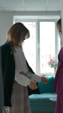 Genç bir kadının arkadaşa yaklaşması ve şık bir ceketle birlikte kıyafet dükkanını ziyaret etmesi. Dikey çekim.