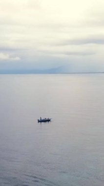 Bulutlu bir gökyüzünün altında sakin bir denizde yüzen teknenin sakin görüntüsü huzur hissi uyandırıyor. Dikey görüntüler