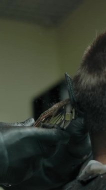 Saç kesiciyle kuaförden müşteriye saç kesiminin yakın çekimi. Çerçevede sadece bir yüz var, müşteri yüzü görünmüyor. Modern berber dükkanı, küçük işletme açılış konsepti. Dikey çekim.