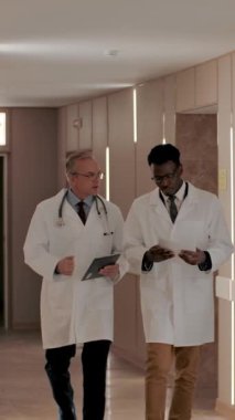 İki mesleki terapist hastane koridorunda yürüyorlar ve bir hastanın geçmişini tartışıyorlar. İki uzman arasında profesyonel bir tartışma. Koyu tenli ve yetişkin beyaz erkekler. Dikey
